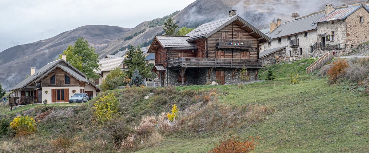 A mountainous village with wooden houses and a car parked in front.