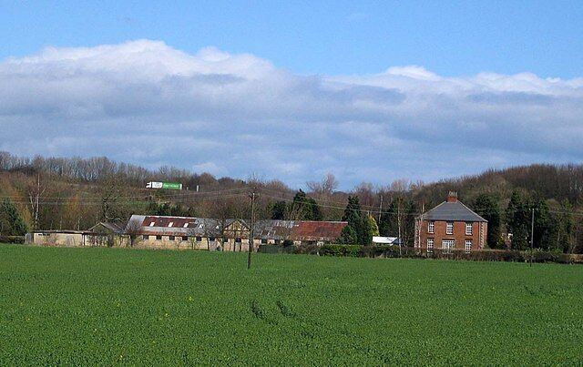 A green field, a brick house, and a building with a red roof.