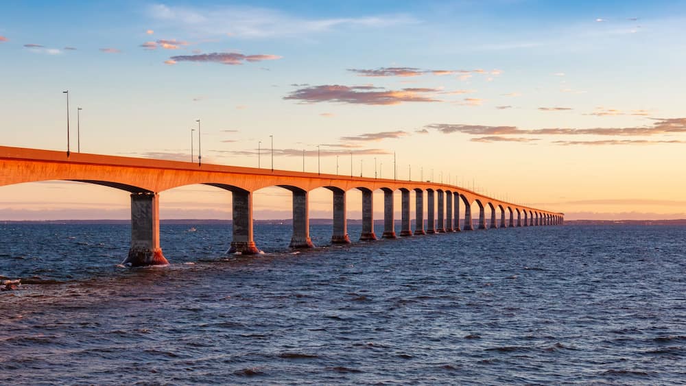 A long bridge with multiple arches extending over a body of water during sunset.