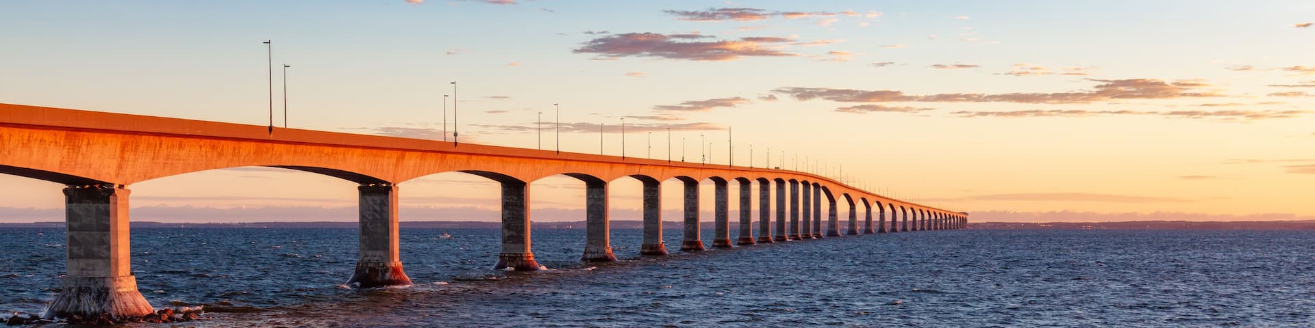 A long bridge with multiple arches extending over a body of water during sunset.