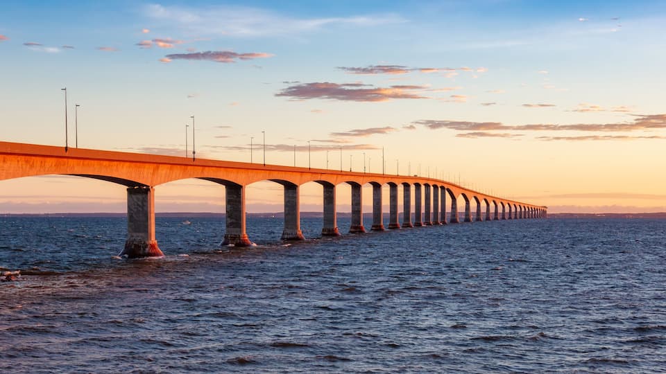 A long bridge with multiple arches extending over a body of water during sunset.
