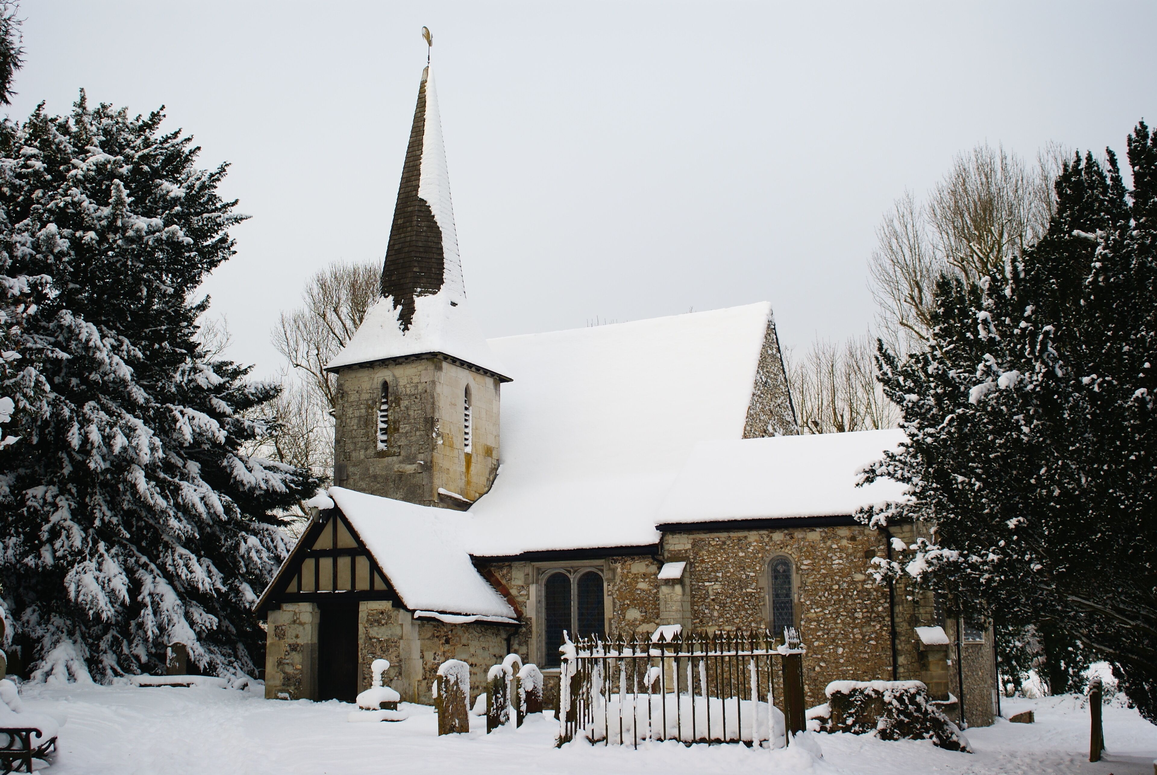A snow-covered church with a steeple and stone walls.