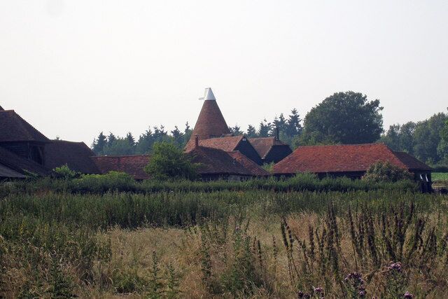 A rural landscape with traditional red-roofed buildings, a distinctive conical structure, and a field in the foreground.