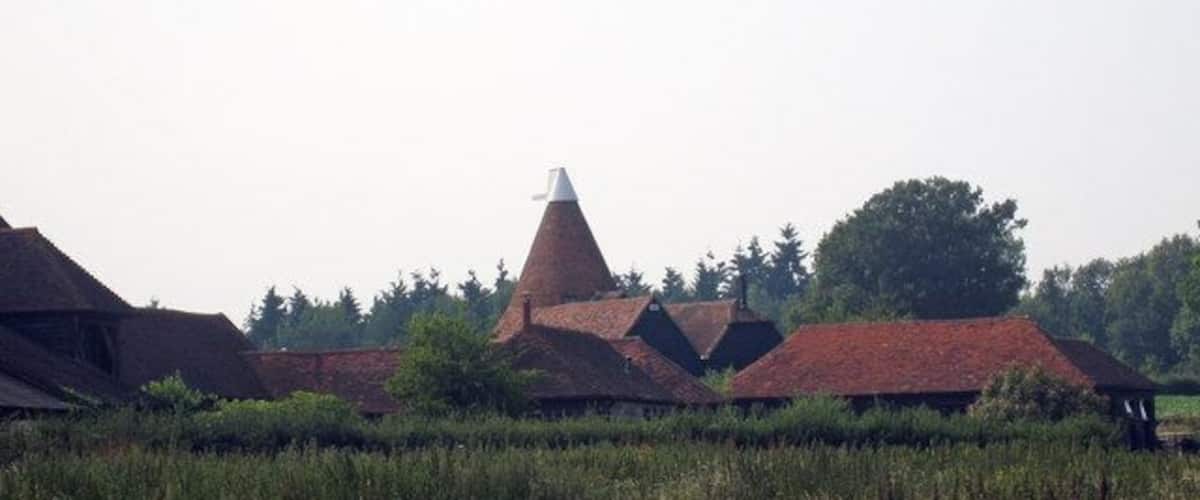 A rural landscape with traditional red-roofed buildings, a distinctive conical structure, and a field in the foreground.