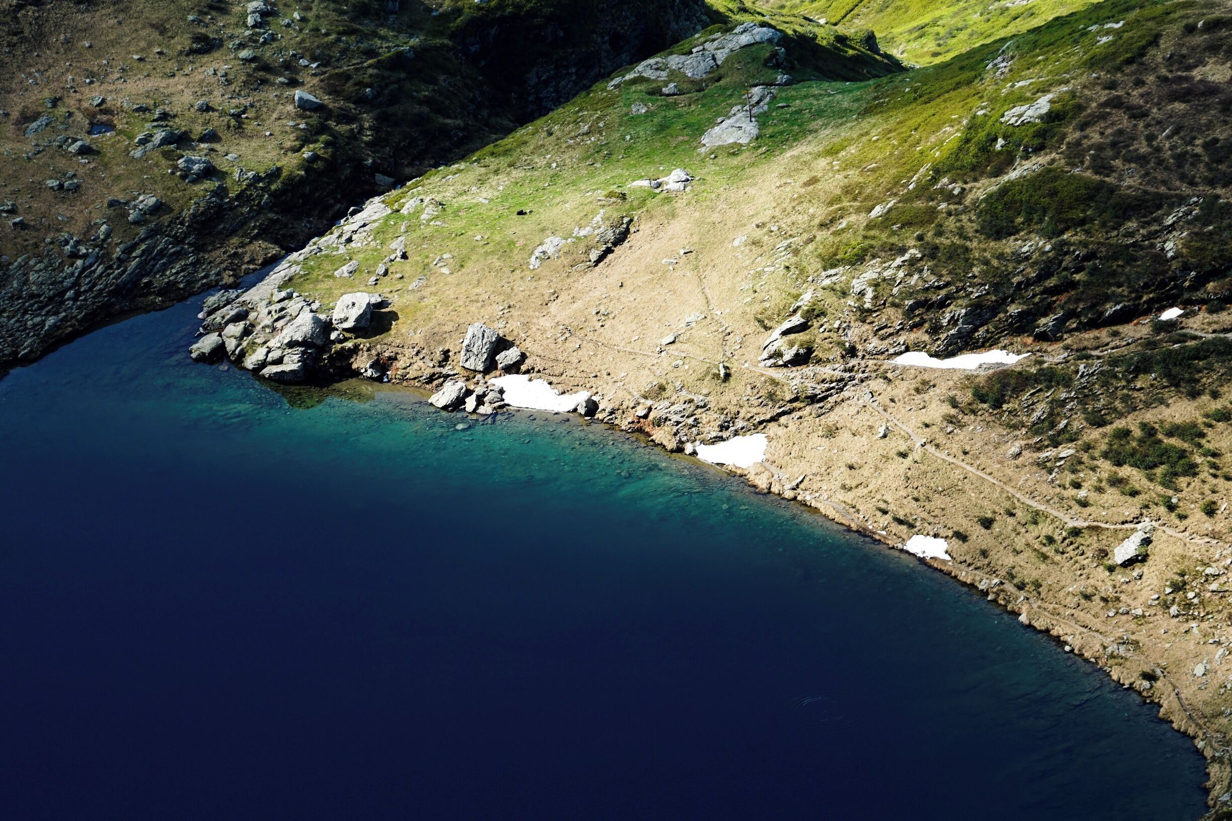 A coastal landscape with a clear blue sea, rocky terrain, and patches of snow.