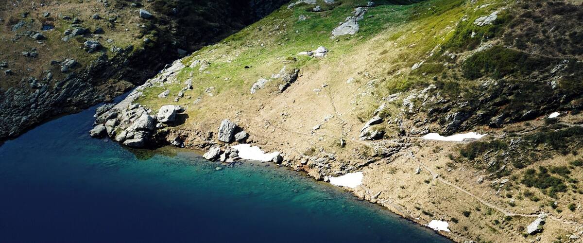 A coastal landscape with a clear blue sea, rocky terrain, and patches of snow.