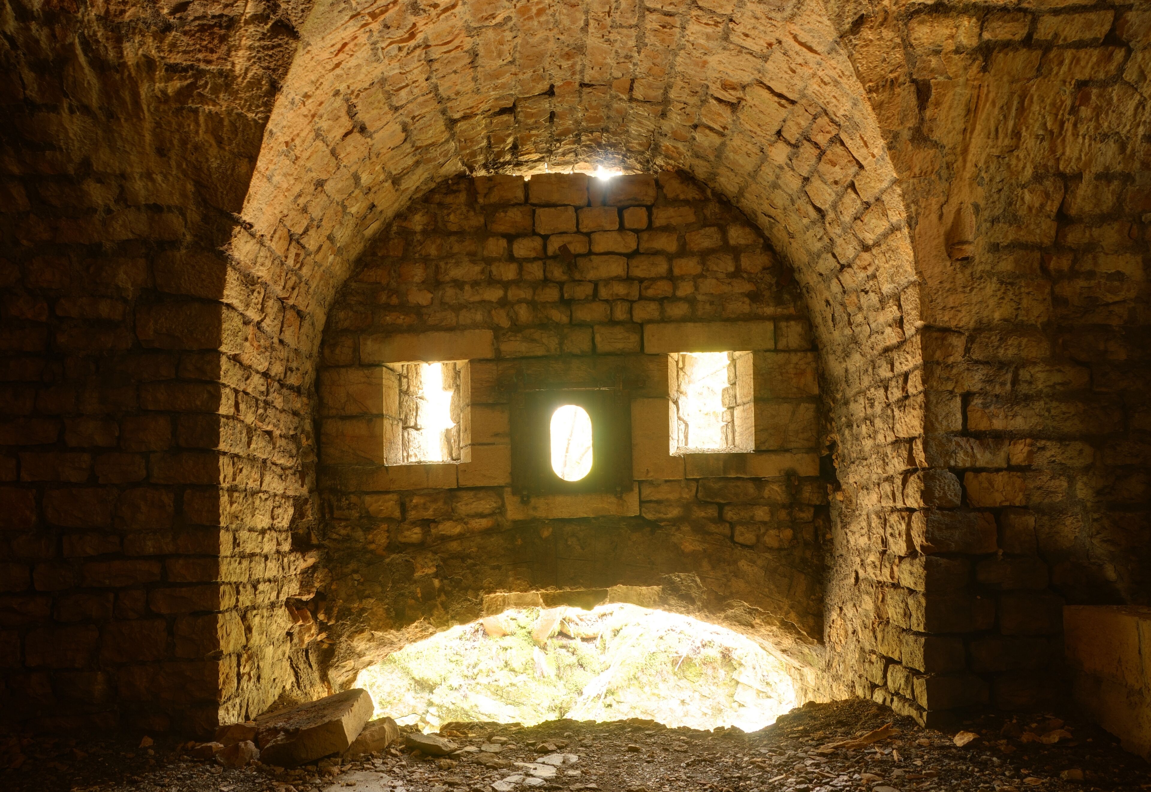 An arched stone structure with two small windows and a central light source.