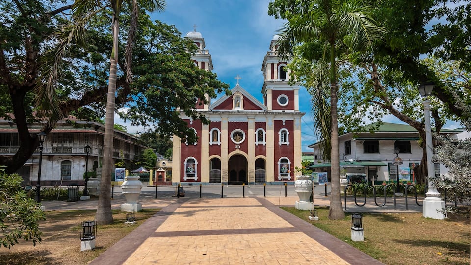 A historic church with a central dome and two bell towers, surrounded by palm trees and a paved walkway.