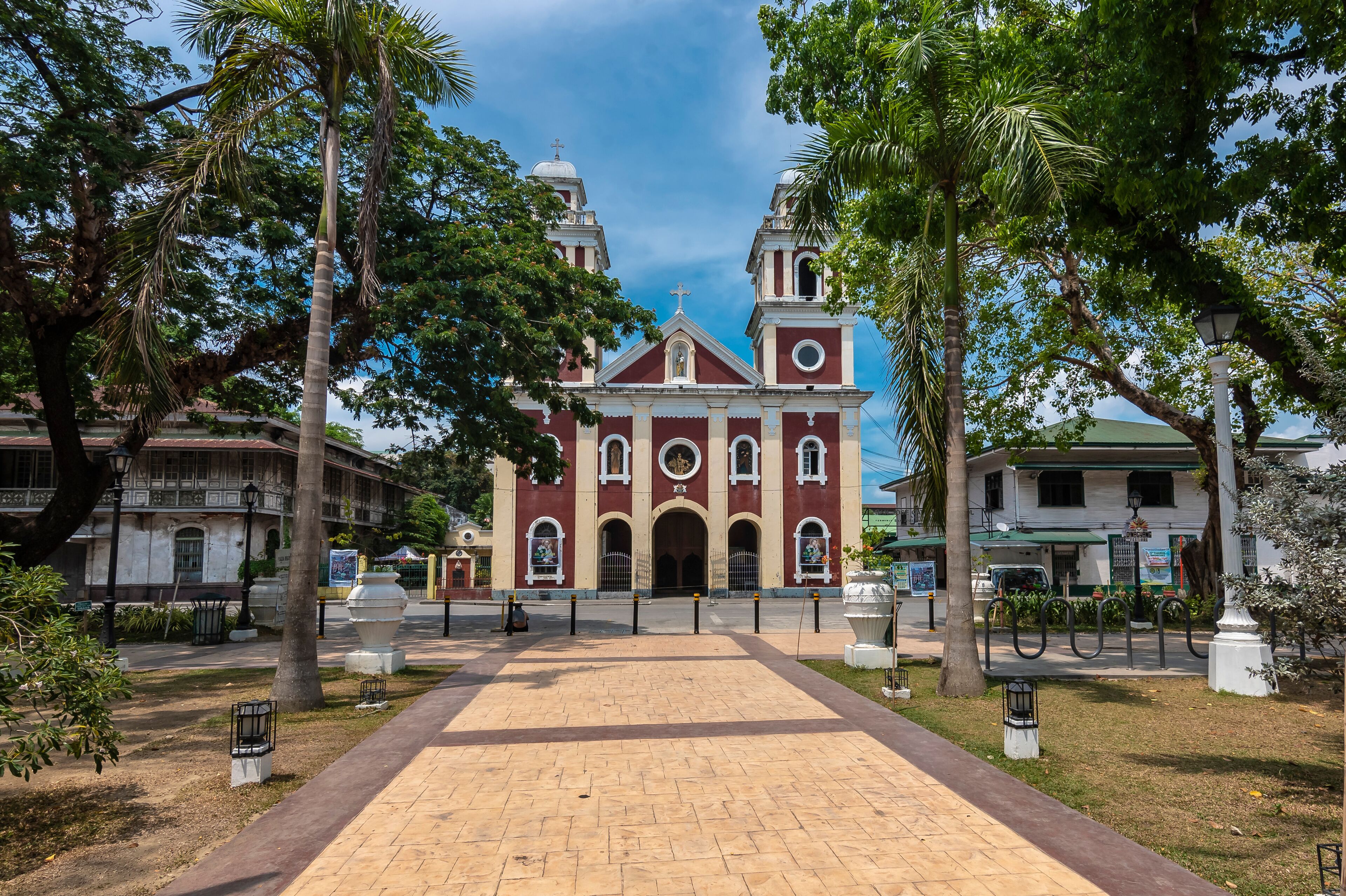 A historic church with a central dome and two bell towers, surrounded by palm trees and a paved walkway.