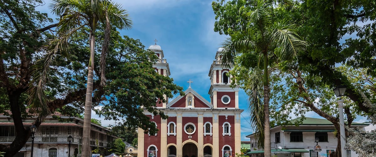 A historic church with a central dome and two bell towers, surrounded by palm trees and a paved walkway.