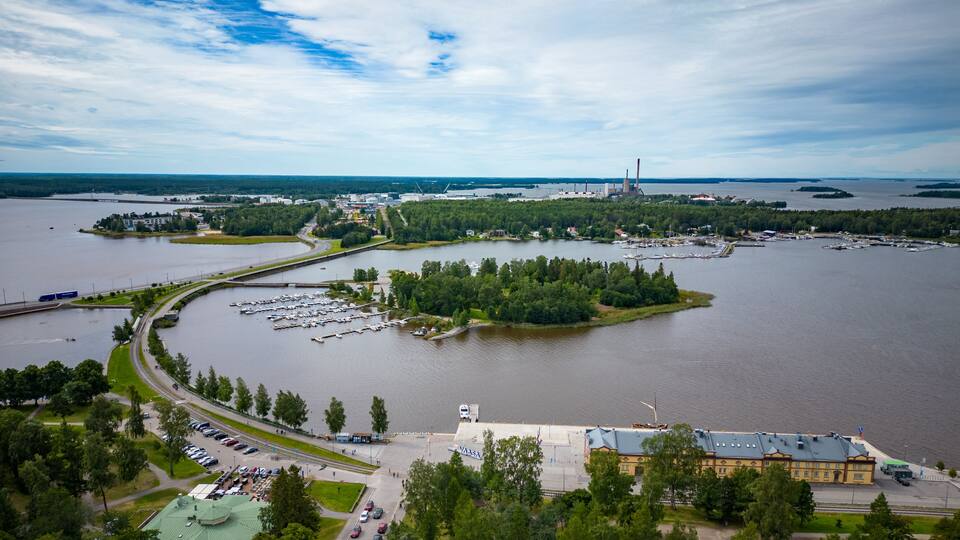 A large body of water with a marina, industrial buildings, and a forested island.