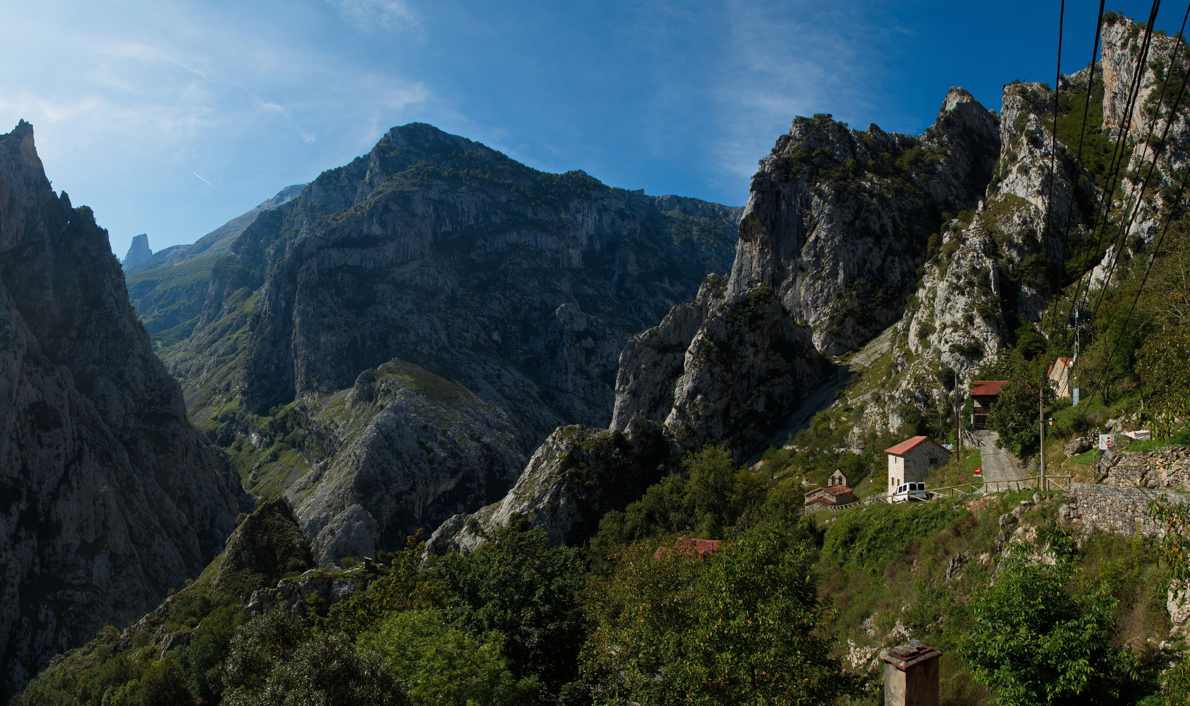Un paysage montagneux avec de hautes falaises rocheuses, un petit bâtiment doté d’un toit rouge et un fourgon garé sur une route étroite.
