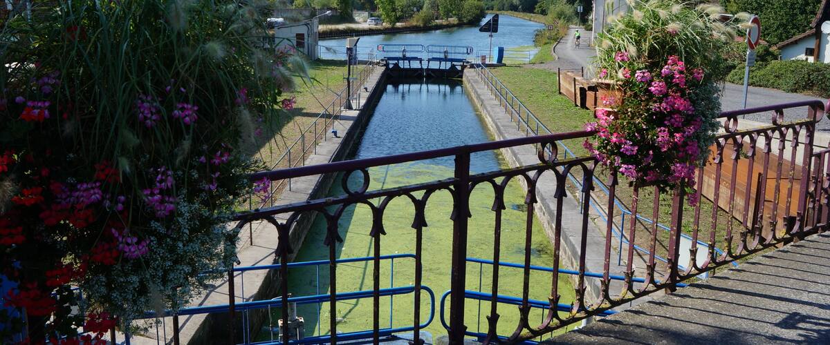 A canal with a lock, surrounded by greenery and houses.