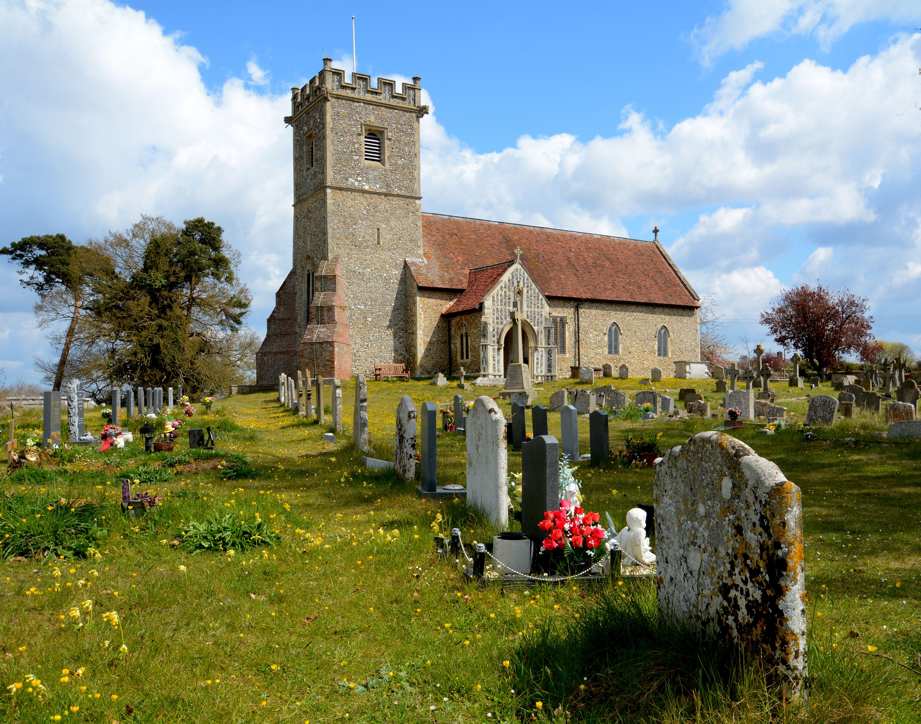 A church with a tall tower and a cemetery with gravestones and flowers.