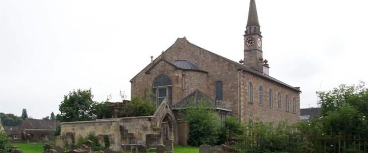 An old church with a tall steeple and numerous gravestones in the foreground.