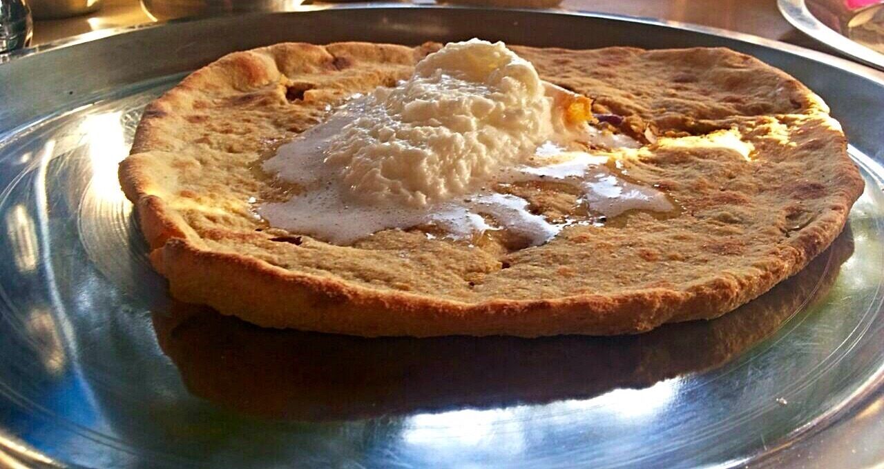 A flatbread with a dollop of white sauce on a metal plate.