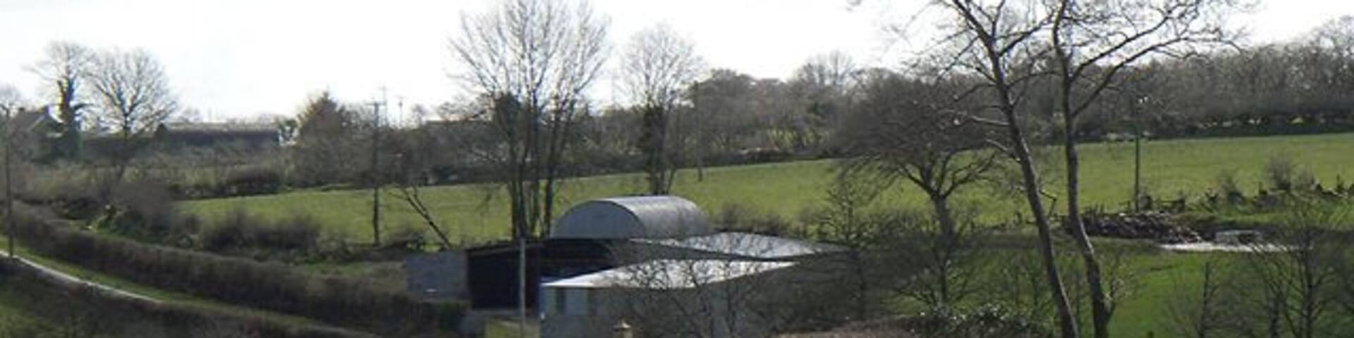 A rural road curving through a countryside with hay bales, a stone wall, and a building in the background.