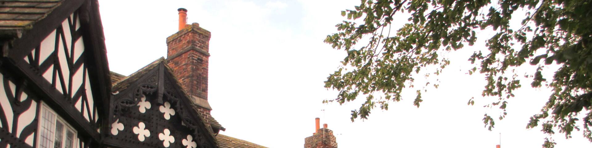 A Tudor-style building with black and white timber framing, brick chimneys, and a well-maintained garden with hedges and a lawn.