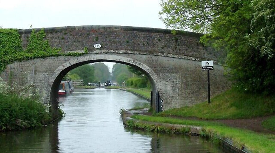 Wheaton Aston Bridge, Staffordshire. This is bridge No 18 on the Shropshire Union Canal, which was opened in 1835 as the Birmingham and Liverpool Junction Canal, engineered by Thomas Telford. Through the arch you will see Wheaton Aston Lock, the first one since the stop lock at Autherley eight miles to the south-east. Telford's policy was to create the shortest canal possible with his technology, building many cuttings and embankments to avoid the alternatives of increasing the distance by meandering along the contours (Brindley's 18th century style) and building locks, both of which would have slowed traffic considerably. Railways were, at that time, taking an increasing amount of the canal companies' business.