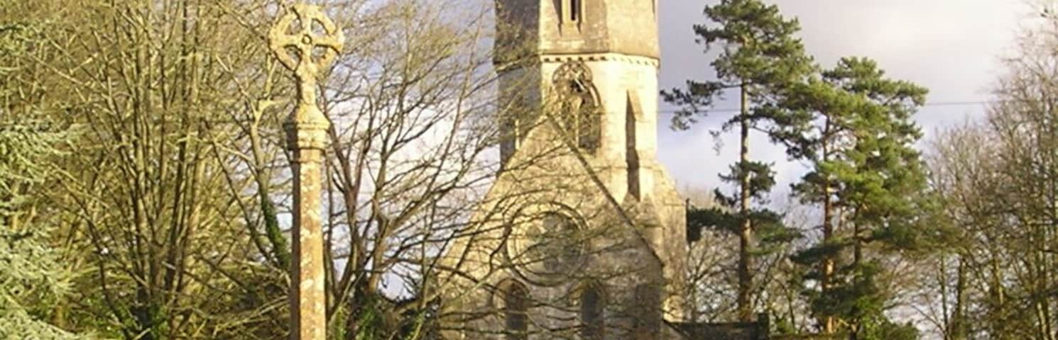 Leafield, Oxfordshire: village cross, with the spire and west end of St Michael and All Angels' parish church in the background. The base of the cross is probably 15th-century. The current shaft and top are a monument thanking God for Leafield's deliverance from an outbreak of smallpox in 1873.