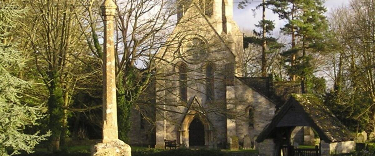 A church with a tall spire and a standing stone in the foreground.