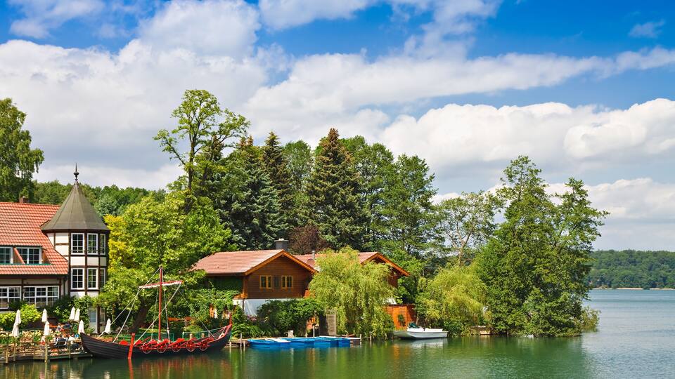 A lakeside village with traditional houses, a wooden boat, and a tower.