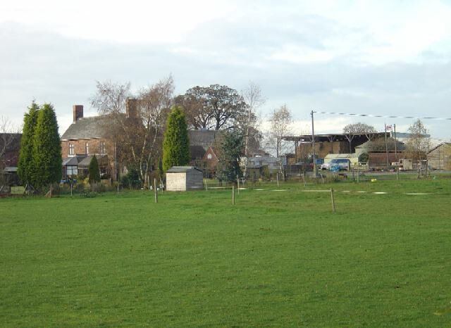 A grassy field with houses and trees in the background.