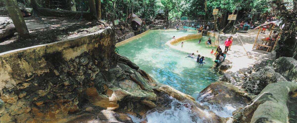 A natural hot spring with clear water surrounded by rocky terrain and trees.