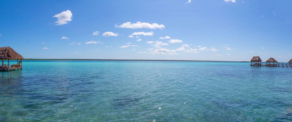 A clear blue sea with overwater bungalows and a thatched-roof structure.