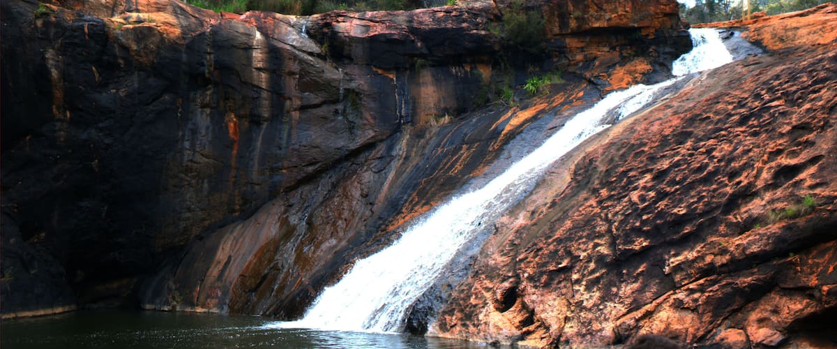 A multi-tiered waterfall cascading down a rocky cliff surrounded by greenery.