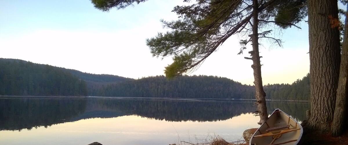A calm lake with a small boat tied to a tree on the shore, surrounded by forested hills.