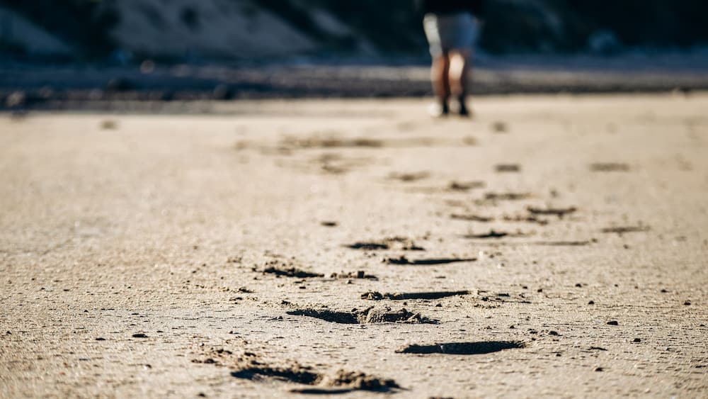 Une plage de sable où l’on voit des empreintes qui mènent à une personne se tenant au loin.