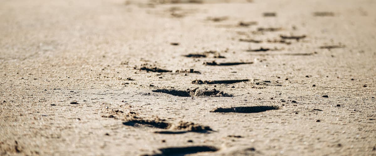 A sandy beach with footprints leading towards a person standing in the distance.