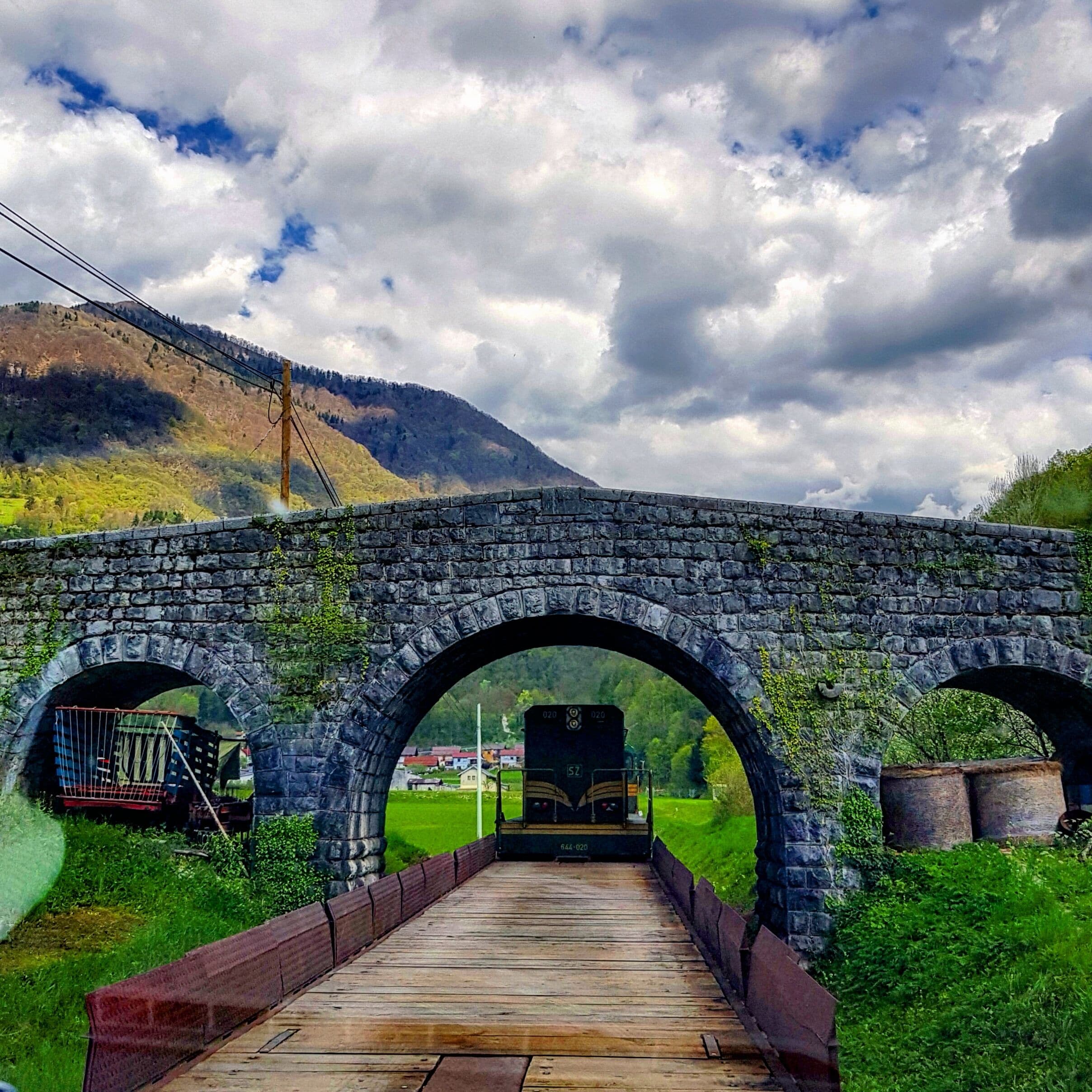 A stone bridge with two arches over a wooden pathway.