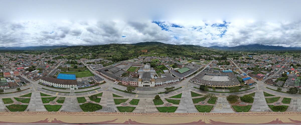 An aerial view of a city with a central plaza, surrounding buildings, and a mountainous backdrop.