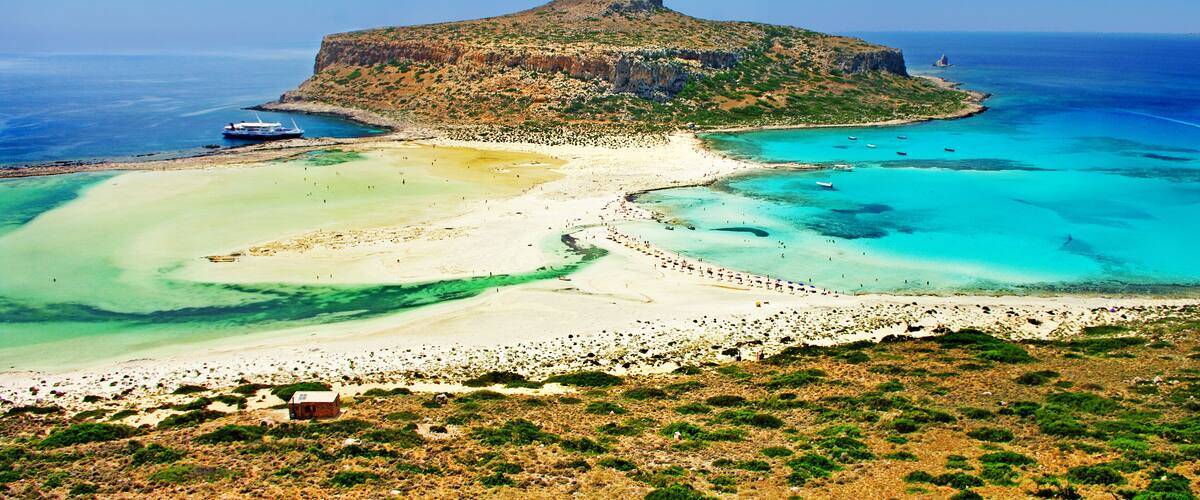 A coastal landscape with a prominent hill, clear turquoise waters, and a sandy beach.