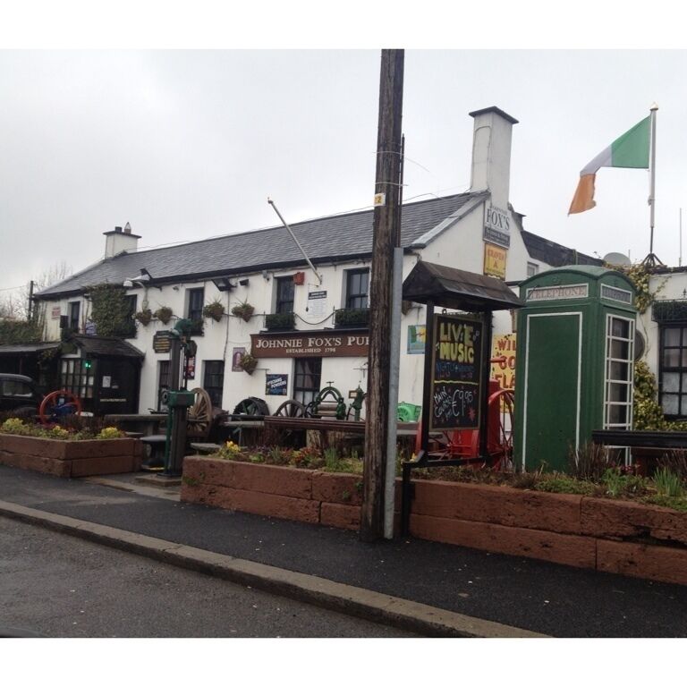 A pub named 'Johnnie Fox's Pub' with a traditional white facade, a green telephone booth, and a flag.