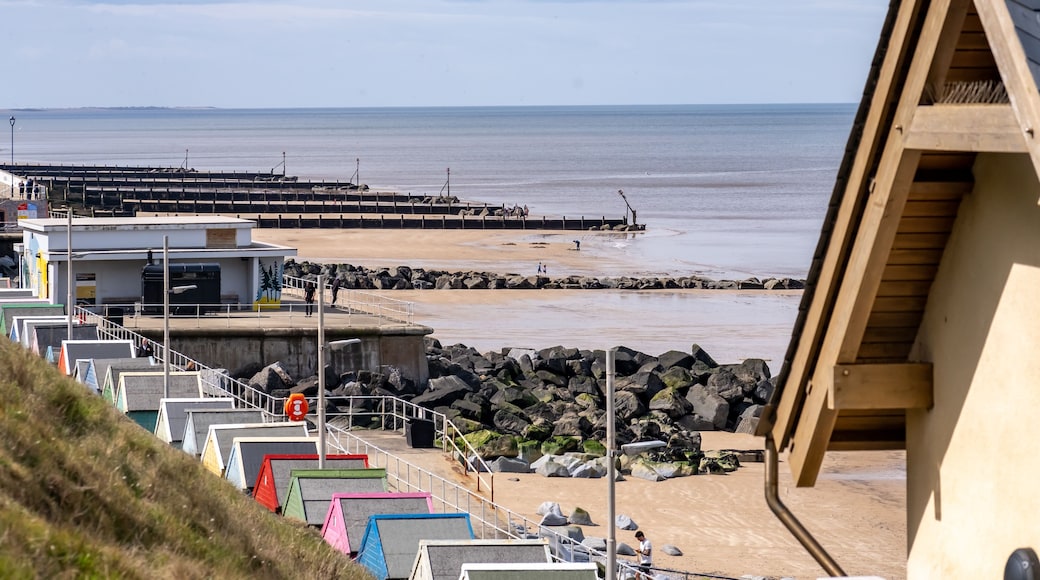A beach with colorful beach huts, a rocky breakwater, and a clear view of the sea.
