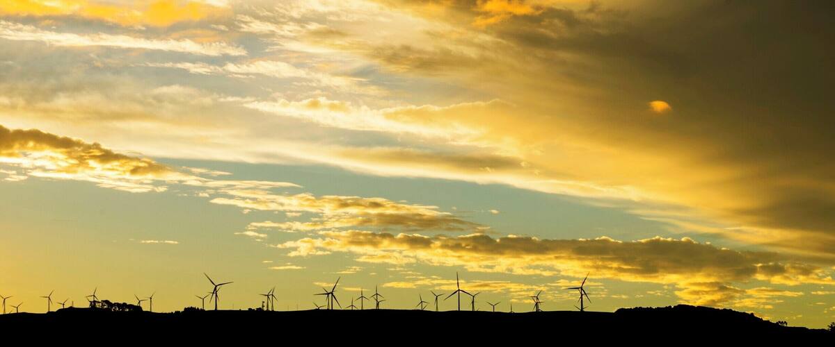 A sunset over a wind farm with multiple wind turbines silhouetted against the sky.