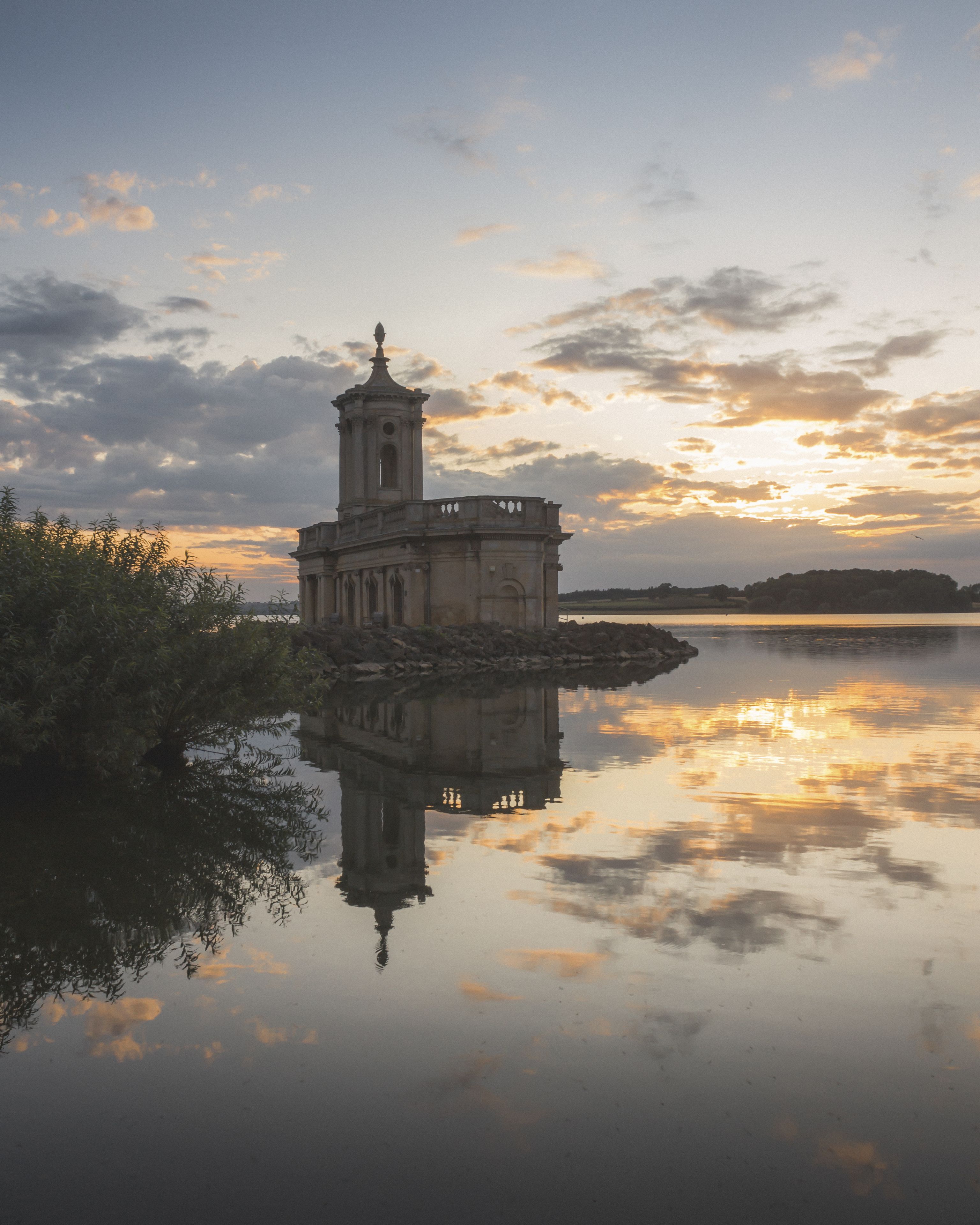 A historic tower by a calm lake with a sunset reflection.