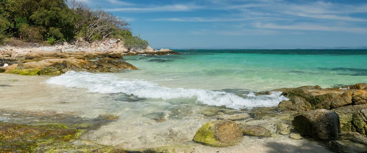 A coastal landscape with clear turquoise waters, rocky shoreline, and dense green foliage.