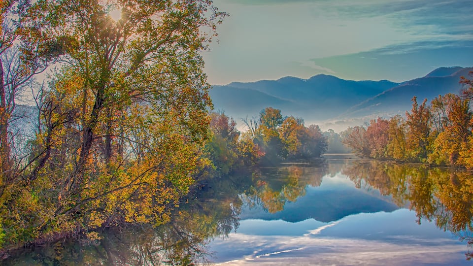 A calm lake reflecting autumn trees and distant mountains.