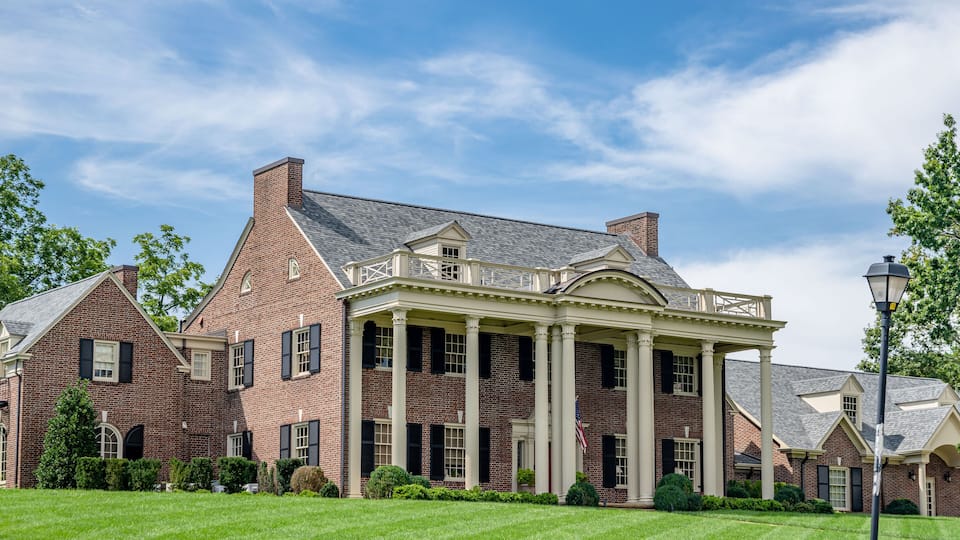 A large brick building with a covered porch and columns, surrounded by well-maintained lawns and trees.