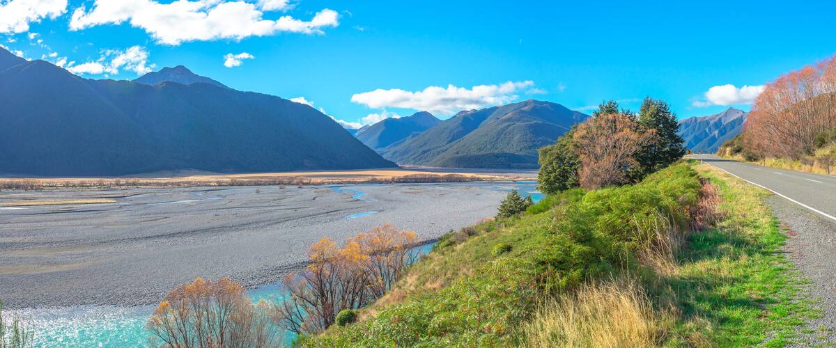 A road with mountains in the background and a river in the foreground.