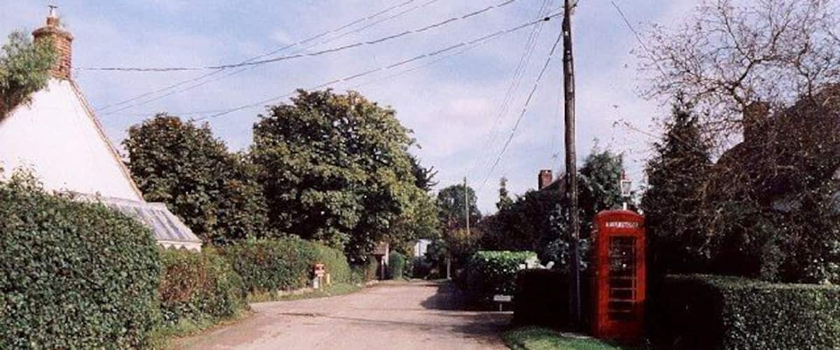 A rural road with a white house, green hedges, and a red telephone booth.