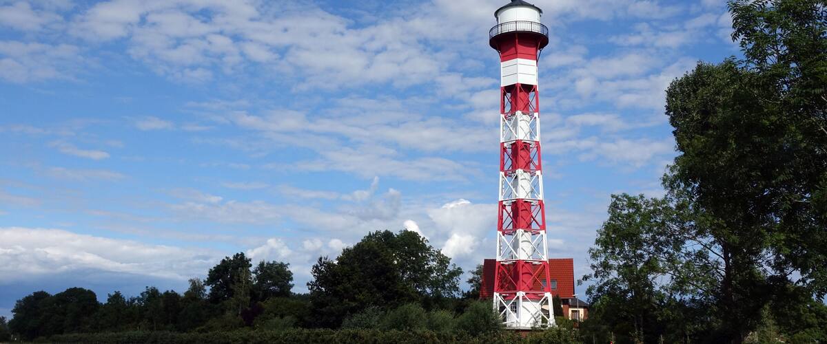 A red and white lighthouse in a grassy field with trees and a clear sky.