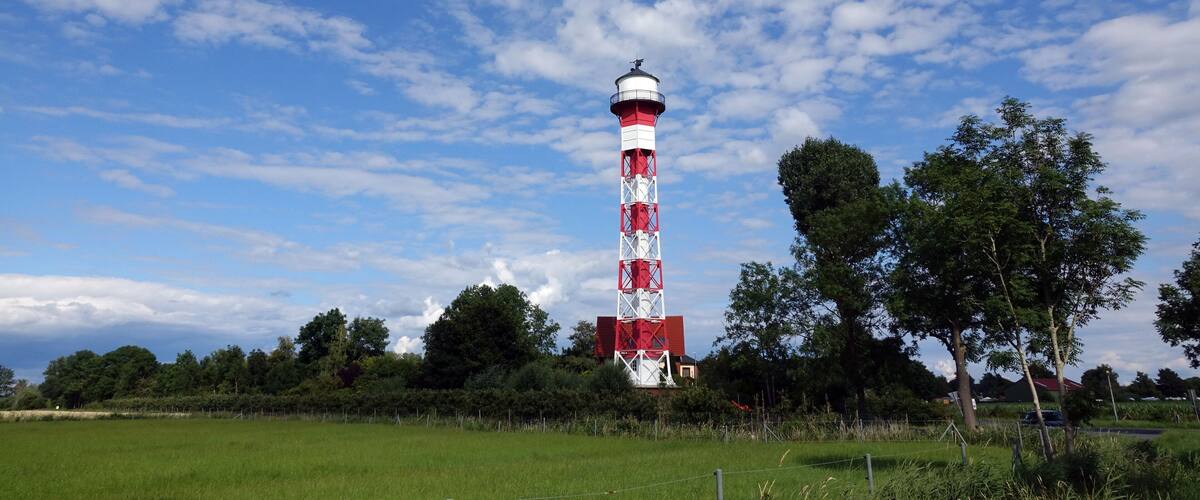 A red and white lighthouse in a grassy field with trees and a blue sky.