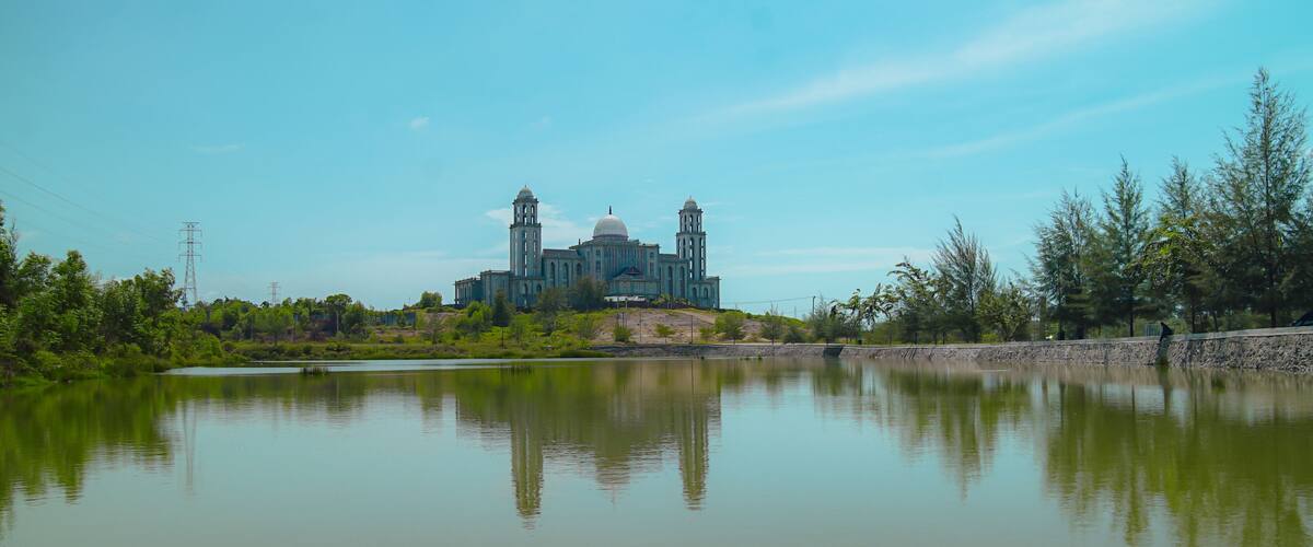 A large building with two towers and a dome, surrounded by a calm lake and greenery.