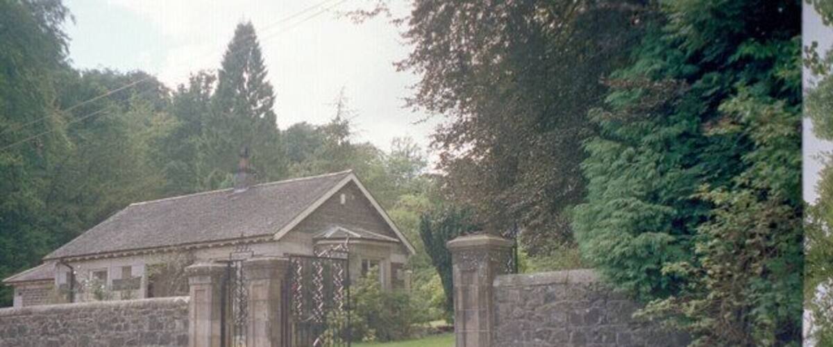 A stone gatehouse with a small building, surrounded by greenery and trees.