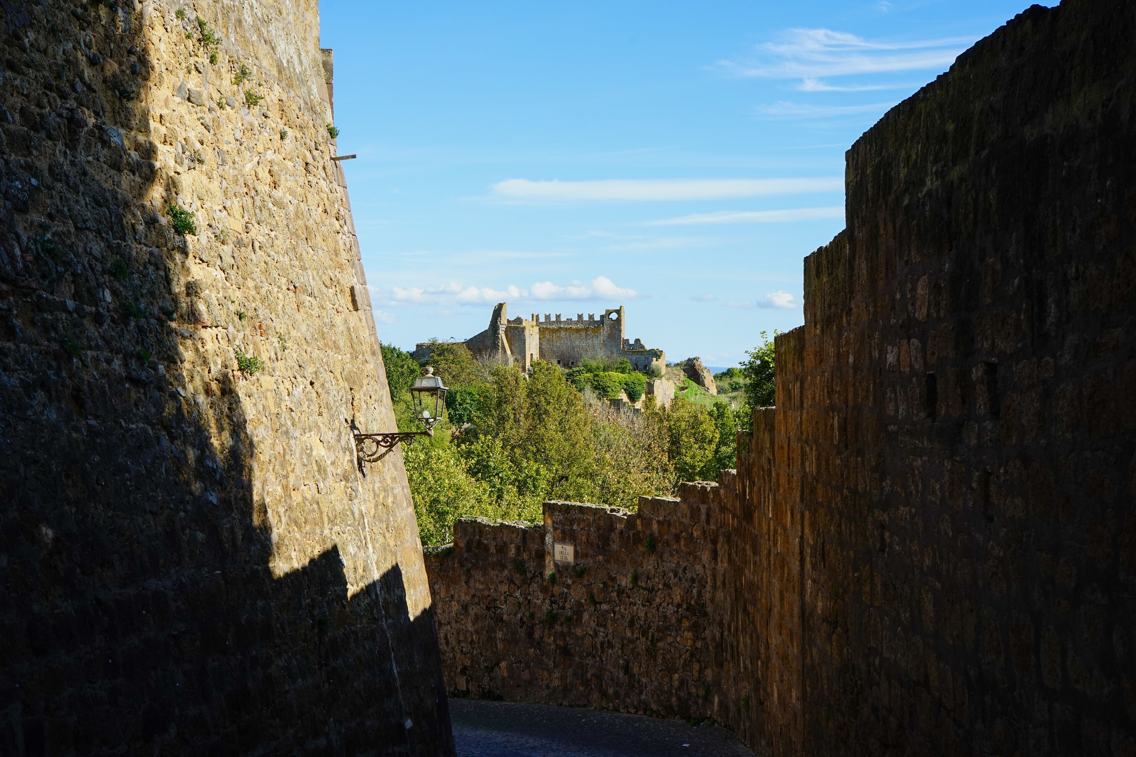 A stone wall with a street lamp and a distant castle.